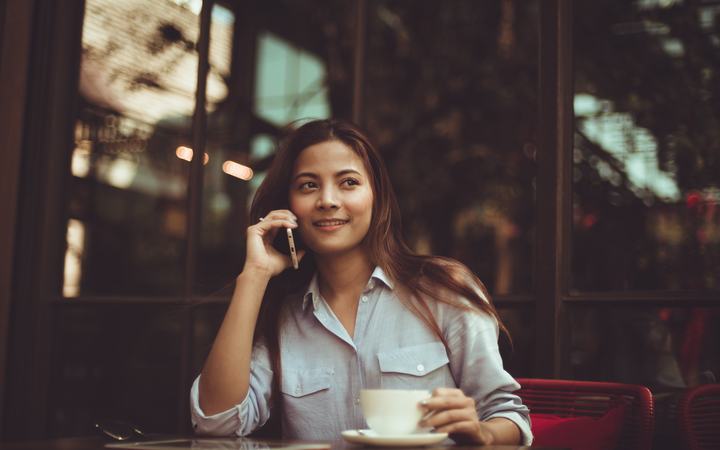 Mujer sonriente atendiendo una llamada desde su teléfono en una cafetería